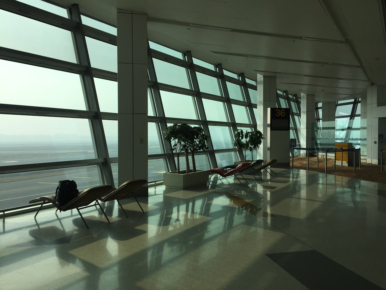 team-02 Sunlit empty terminal at New Delhi Airport with chairs and large windows.