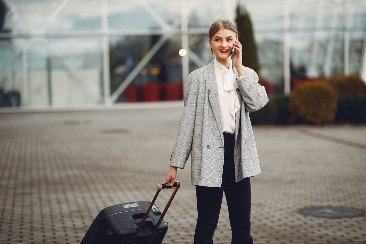 Confident businesswoman walking with luggage while talking on phone at airport terminal.